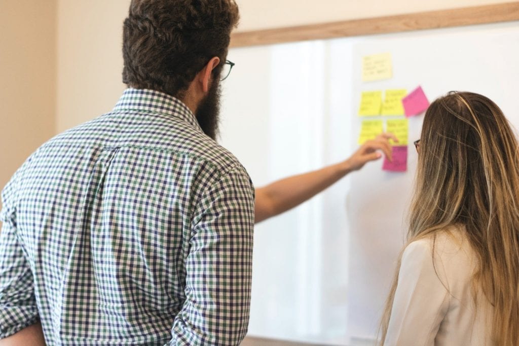 Man placing sticky notes on a whiteboard during a discussion.