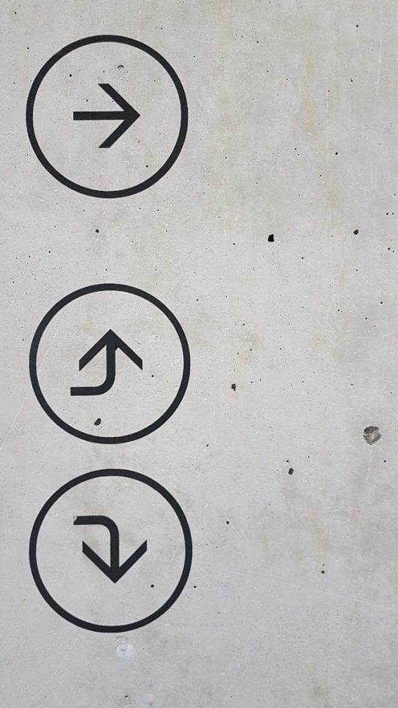 A black upward arrow inside a circle on a concrete surface.